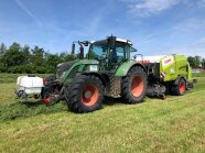 Ein Traktor mit Siloballenpresse und an der Fronthydraulik angebautem Siliermitteldosierer presst auf der Versuchsfläche Siloballen.