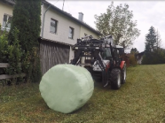Traktor mit Ballenzange beim Aufnehmen eines Siloballens