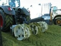 Ein landwirtschaftliches Fahrzeug fährt mit einem angehängten Verdichterrad über die Silage.