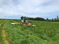 Traktor mit Front- und Heckmähwerk beim Mähen einer Wiese