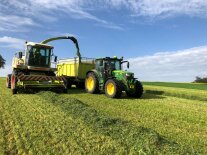 Grashäcksler und Traktor mit Anhänger bei der Grasernte.