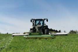 Traktor mit Front- und Heckmähwerken beim Mähen von Grünland