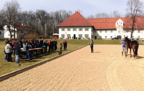 Eine Gruppe von Menschen steht einer Person sowie einer weiteren Person mit Pferd gegenüber