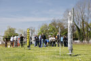 Ein mobiler Zaun auf grüner Wiese im Vordergrund. Im Hintergrund werden die interessierten Zuschauer informiert. 