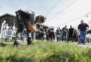 Im Vordergrund ein Landwirt, der einen Festzaun mit Drähten installiert. Im Hintergrund interessierte Zuschauer. 