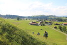 Familie besteigt eine ansteigende Wiese mit Dorf im Hintergrund.
