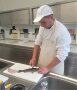 Junger Mann in weißer Arbeitskleidung filetiert einen Fisch.
