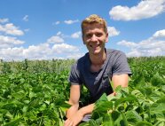 Ein Mann sitzt in der Hocke in einem Feld und lacht