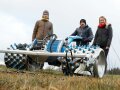 drei Personen stehen hinter einem großen Motormäher