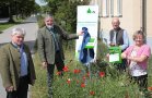 Menschen in einer Blühfläche vor eine Gebäude enthüllen ein Schild