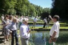 Ein Mann erklärt einer Besuchergruppe etwas an einem Fischteich.