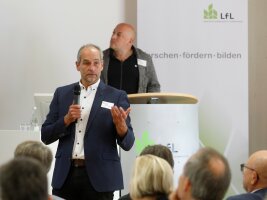 Herr Friedrich spricht mit dem Mikrofon in der Hand vor Konferenzteilnehmern.