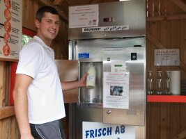 Person in einem Verkaufshäuschen an einem Milchautomaten.