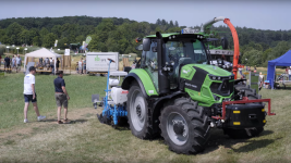 Zwei Besucher und ein Traktor, im Hintergrund Versuchsfelder und Pavillons.