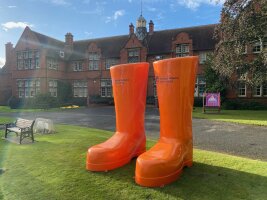 Überdimensionale orangefarbene Gummistiefel vor der Fassade der Harper Adams University.