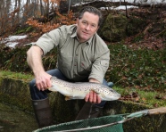 Mann hockt in eine Bach und hält einen großen Fisch